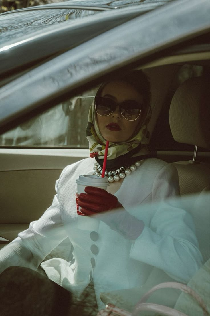 a woman sitting in the back seat of a car holding a drink