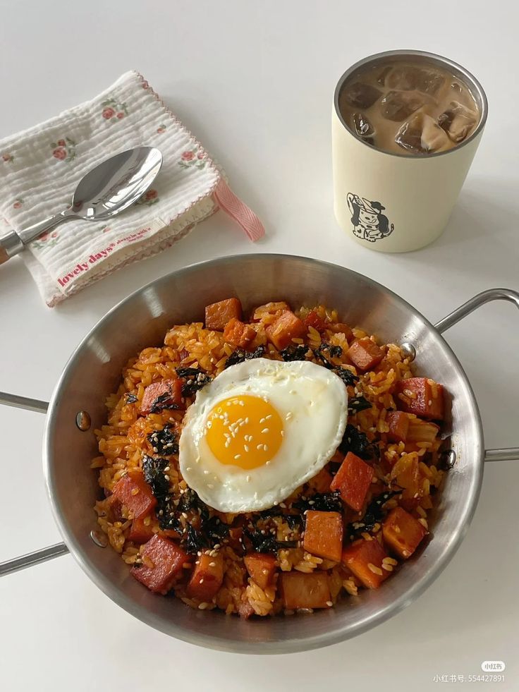 an egg is on top of rice in a pan next to a cup and spoon