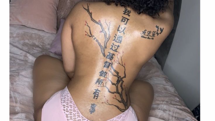 a woman with tattoos on her back sitting on a bed