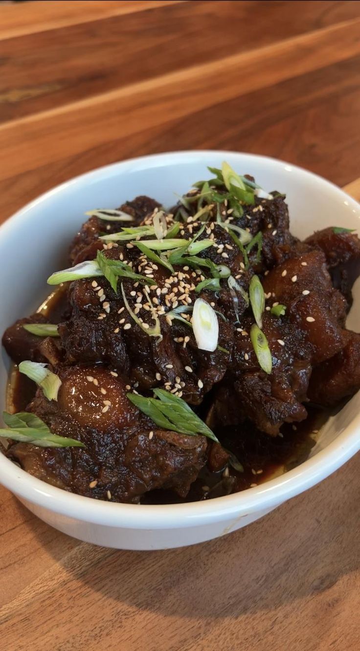 a white bowl filled with meat covered in sesame seeds and garnished with green onions