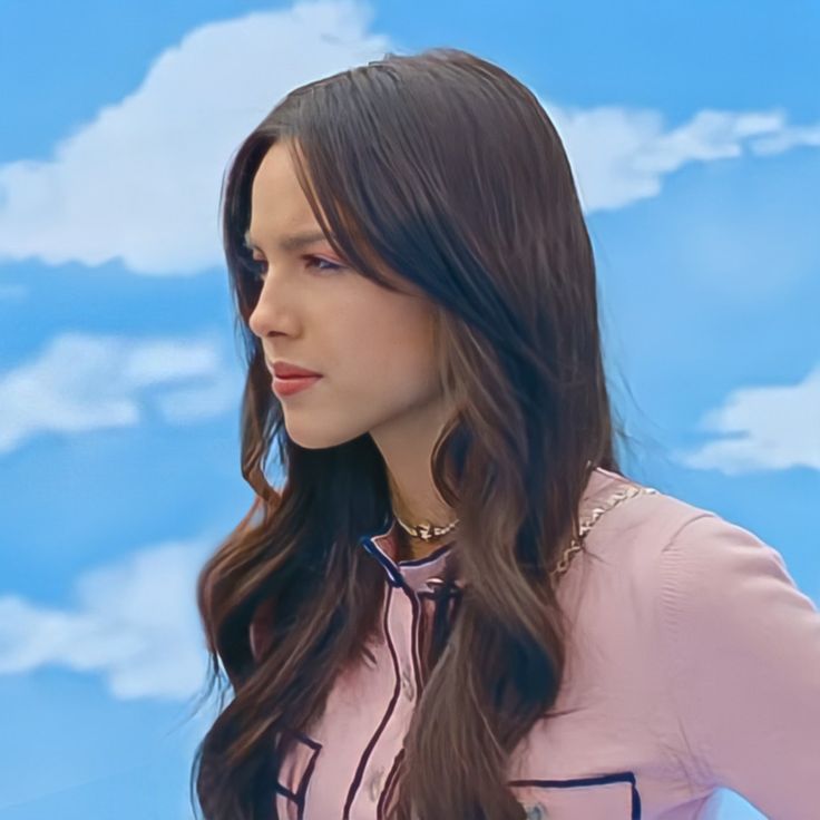 a woman with long hair standing in front of a blue sky and white cloud background