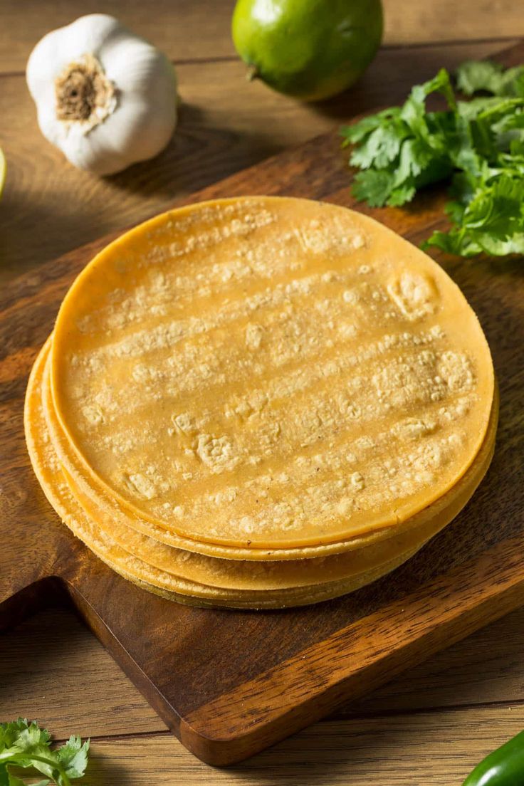 three tortillas on a wooden cutting board next to green peppers and limes