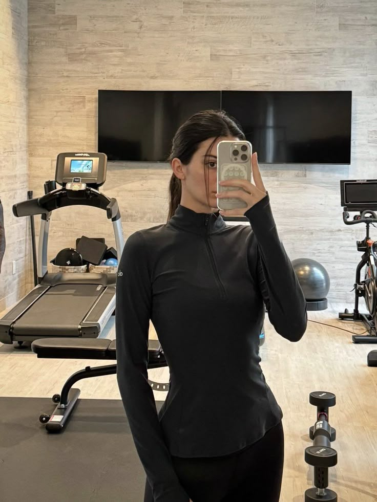 a woman taking a selfie in front of a treadmill with her cell phone