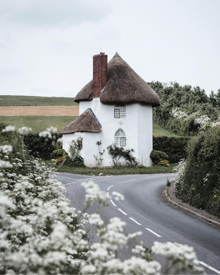 an old white house with a thatched roof in the middle of a country road