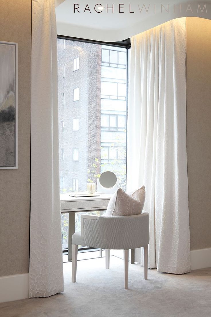 a white chair sitting in front of a window next to a painting on the wall