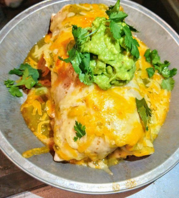 an enchilada dish with guacamole and cilantro on top