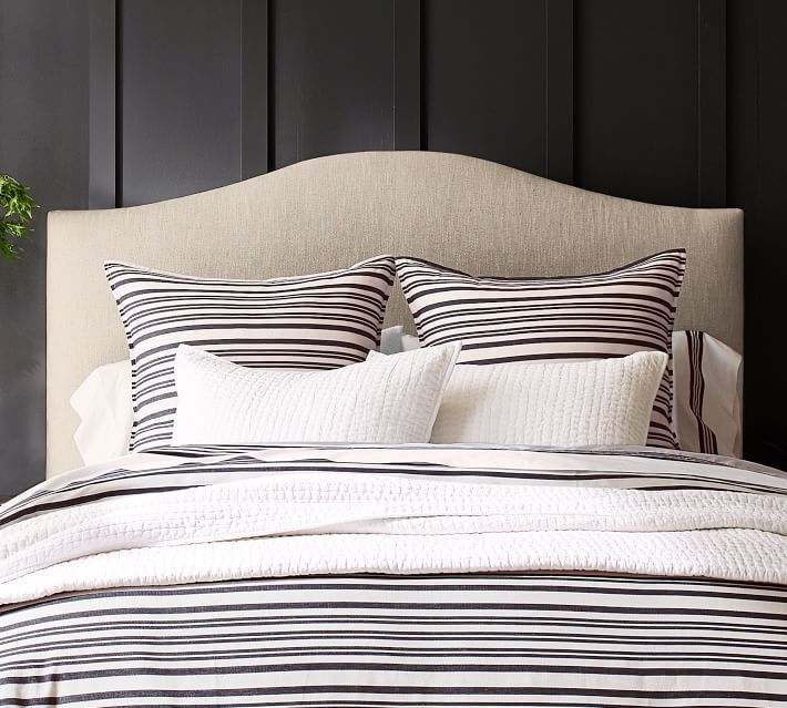 a bed with black and white striped comforter on top of it next to a potted plant