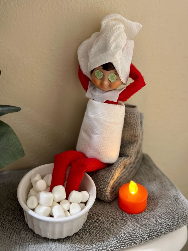 an elf sitting on top of a table next to a bowl of marshmallows