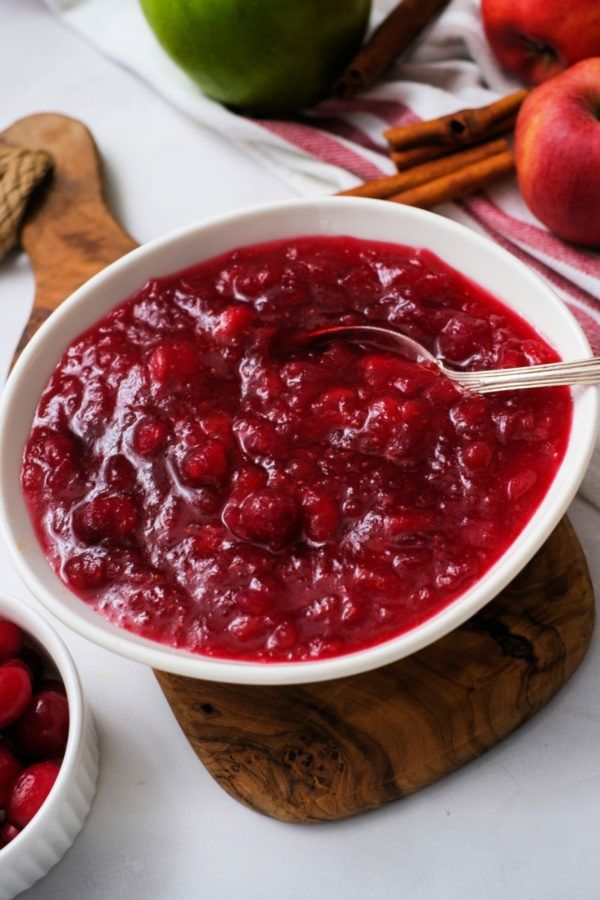 a white bowl filled with cranberry sauce next to apples