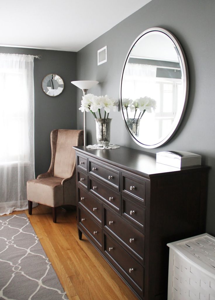 a bedroom with a dresser, mirror and chair