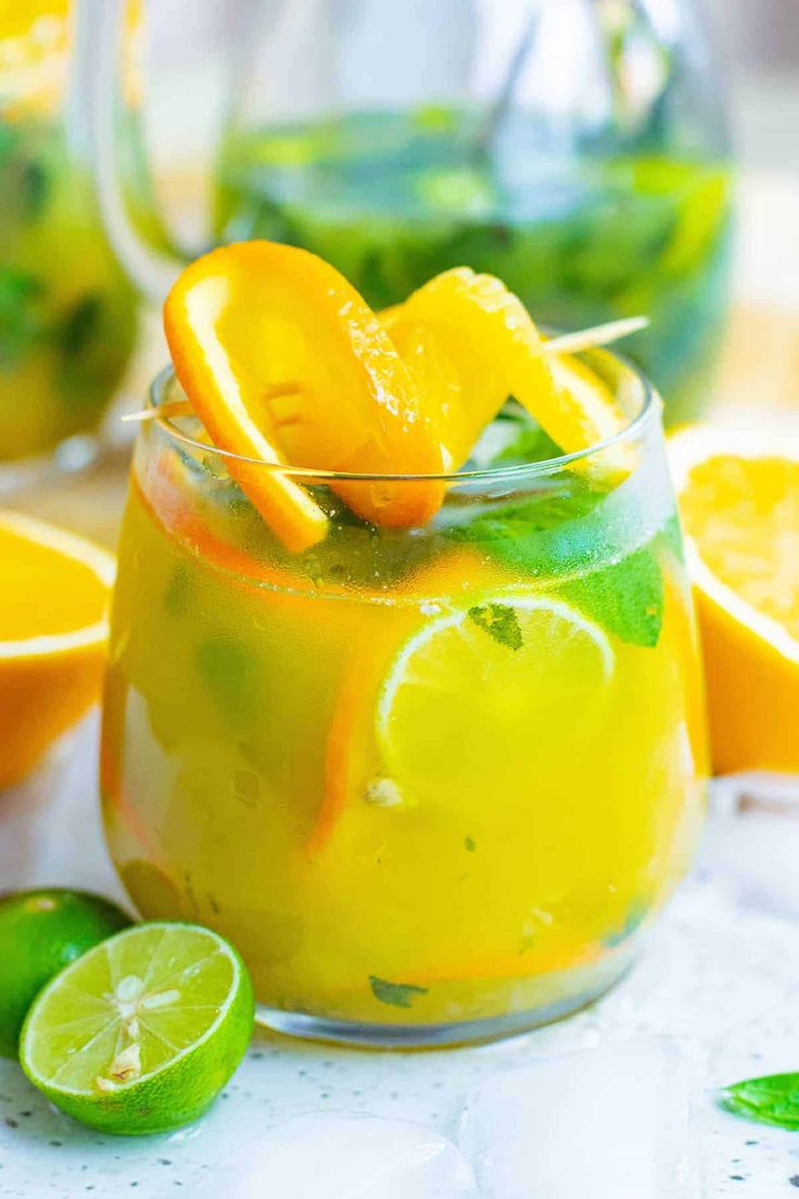 a pitcher filled with lemonade and limes on top of a white tablecloth