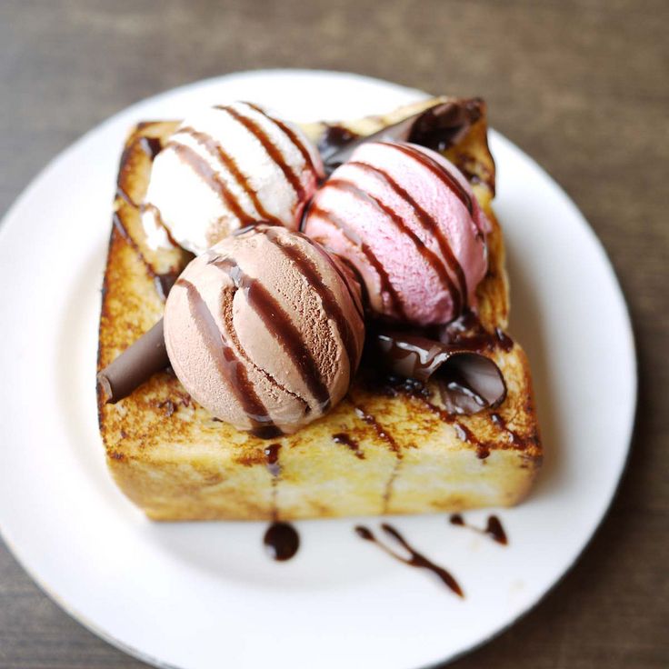 three scoops of ice cream sit on top of toasted bread with chocolate drizzle