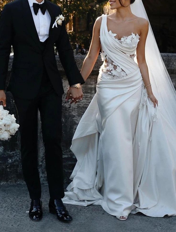 a bride and groom holding hands walking down the street