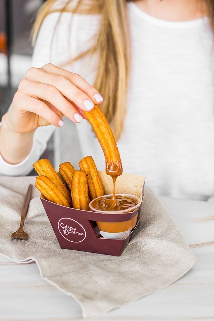 a woman sitting at a table with french fries and dipping sauce on her fingers in a bowl