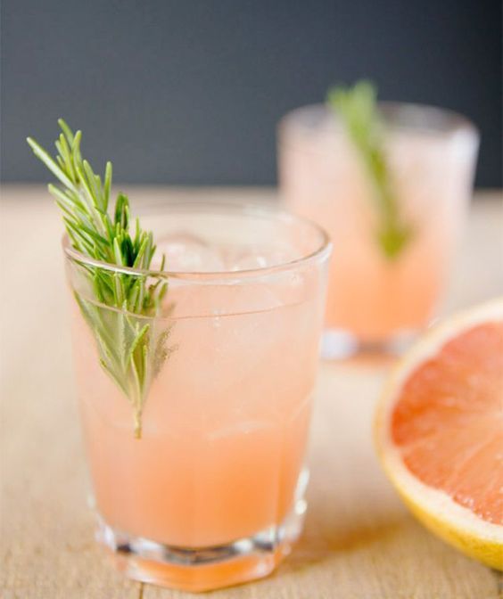 two grapefruit cocktails with rosemary garnish sit on a wooden table