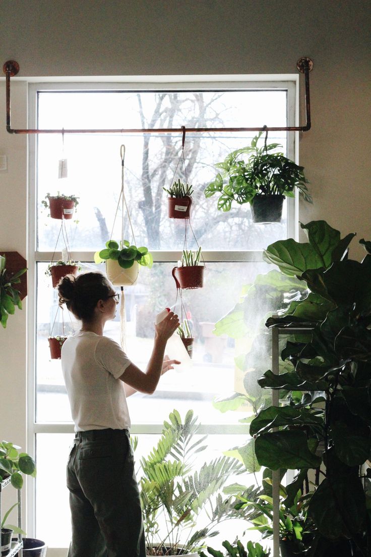 a woman standing in front of a window next to potted plants