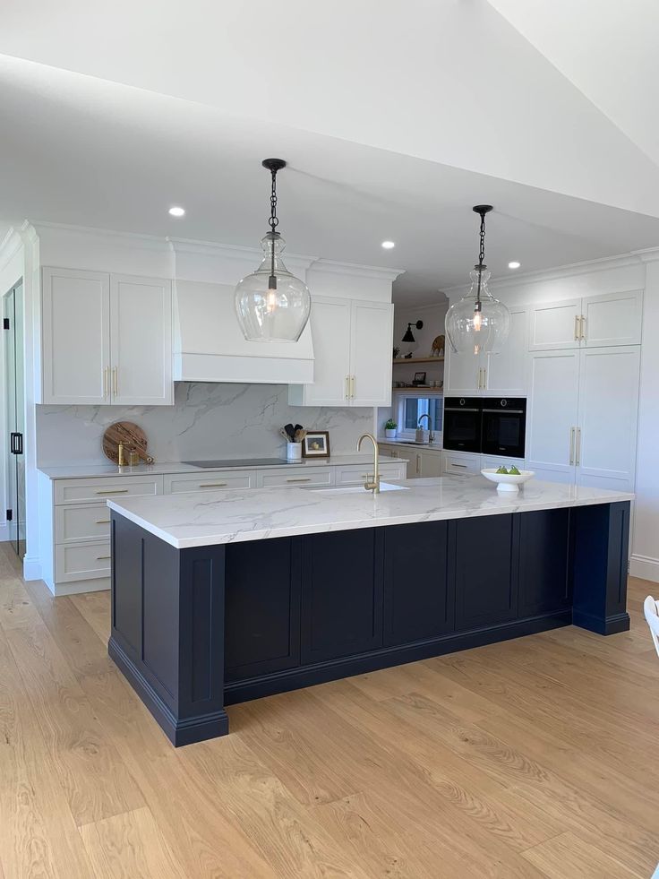 a large kitchen with an island in the middle and two pendant lights hanging from the ceiling