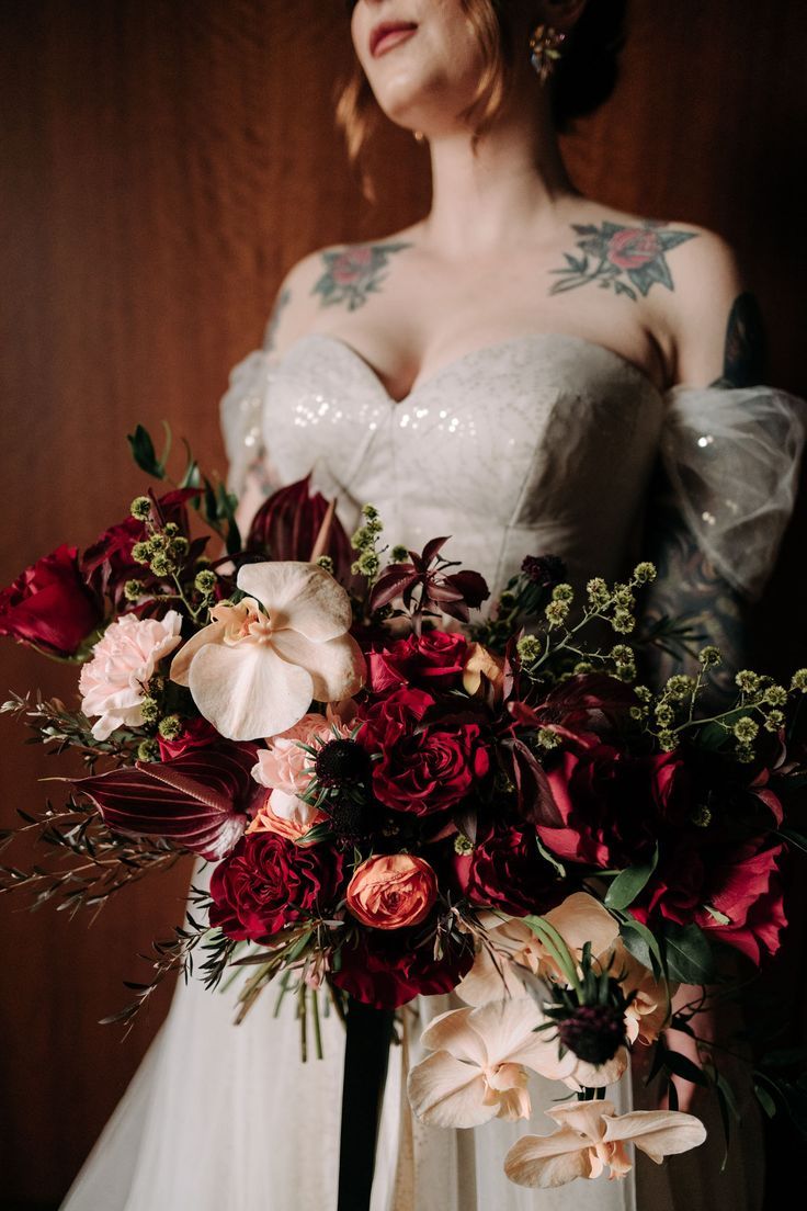 a woman in a wedding dress holding a large bouquet with red and pink flowers on it