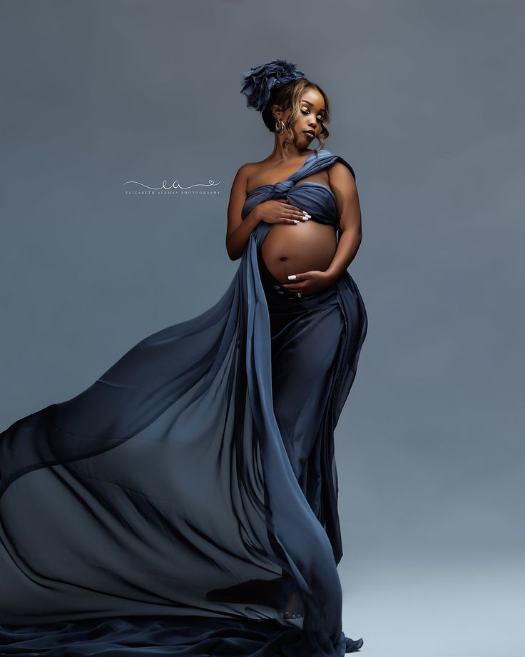 a pregnant woman in a blue dress poses for the camera with her belly wrapped up