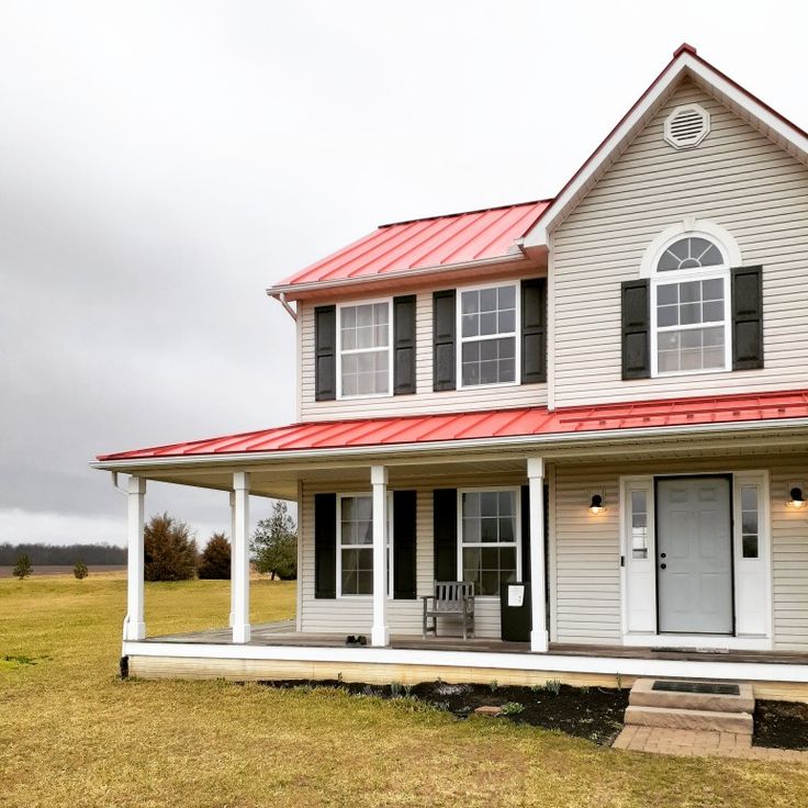 a white house with a red metal roof and two porches on the front lawn