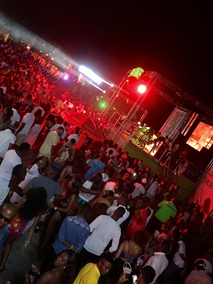 a large group of people standing around in front of a stage at night with red lights