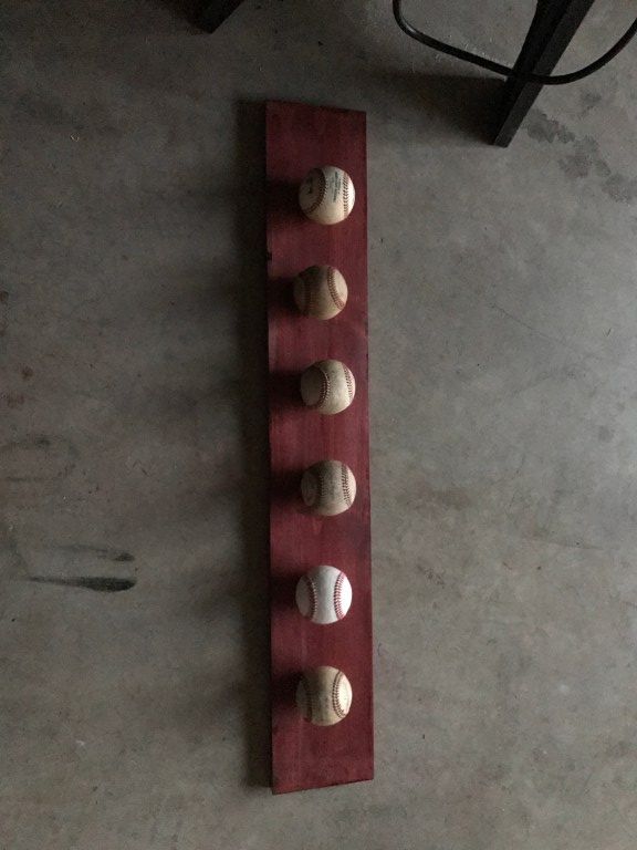 a wooden rack with baseballs in it on the floor next to a chair and table