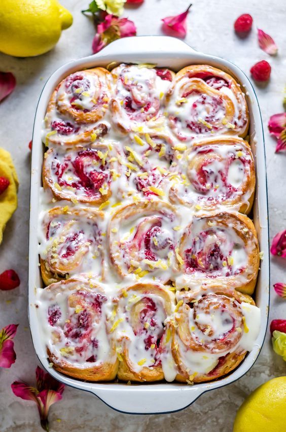 a pan filled with rolls covered in icing next to lemons and strawberries