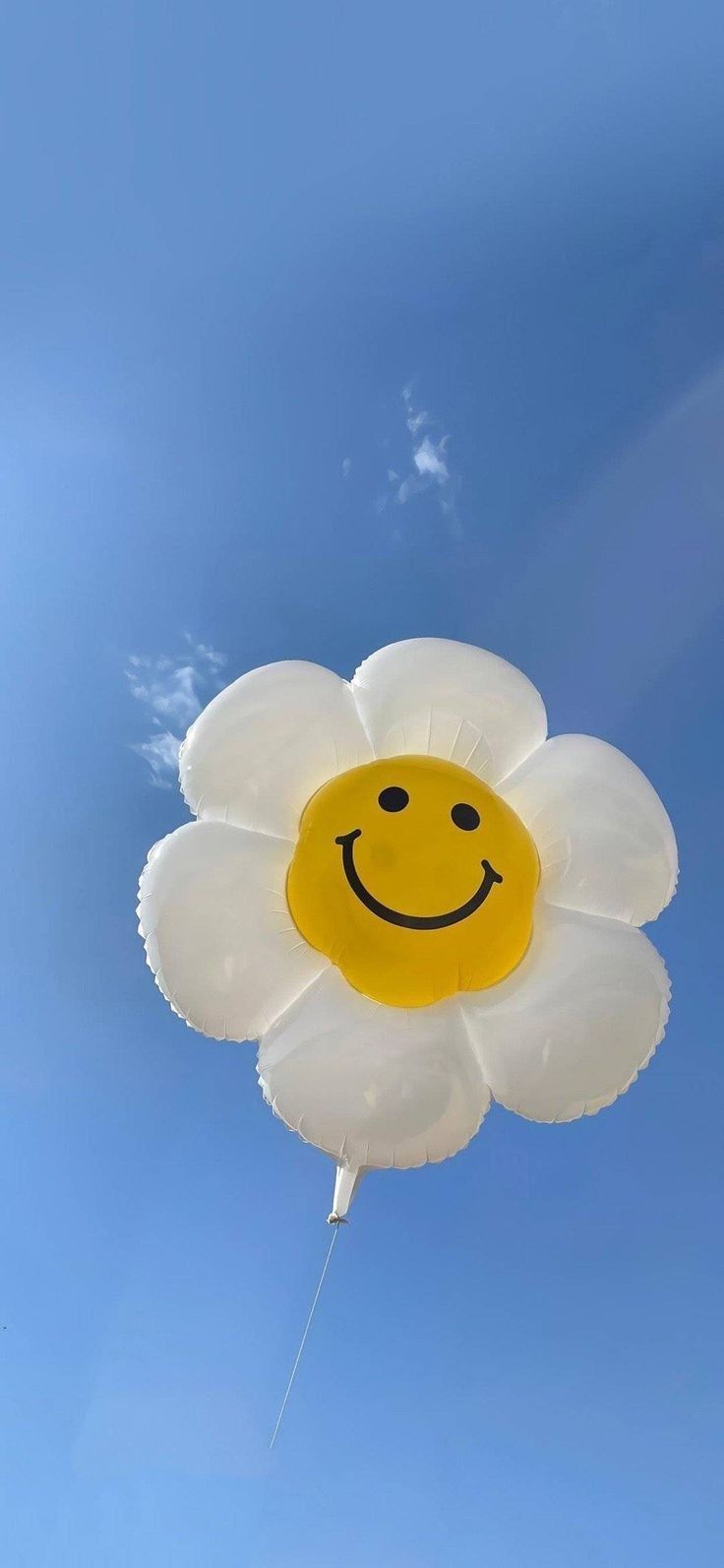 a yellow and white balloon with a smiley face drawn on it's side flying in the air