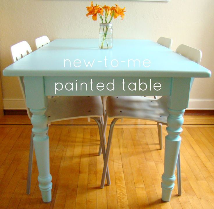 a blue table with white chairs and flowers in a vase on top of the table