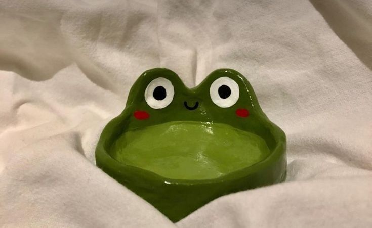 a green frog sitting in the middle of a white sheet with its eyes wide open