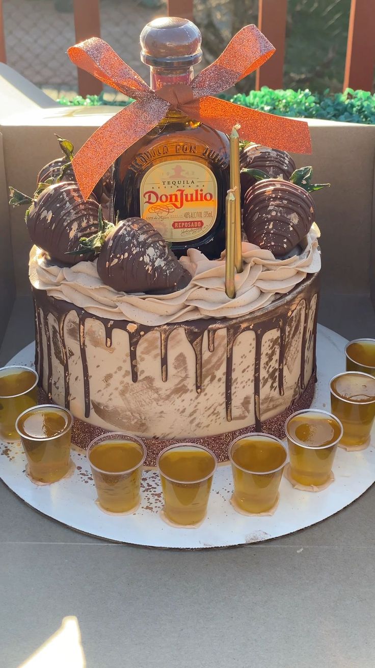 a cake with chocolate frosting and strawberries on top, surrounded by shot glasses