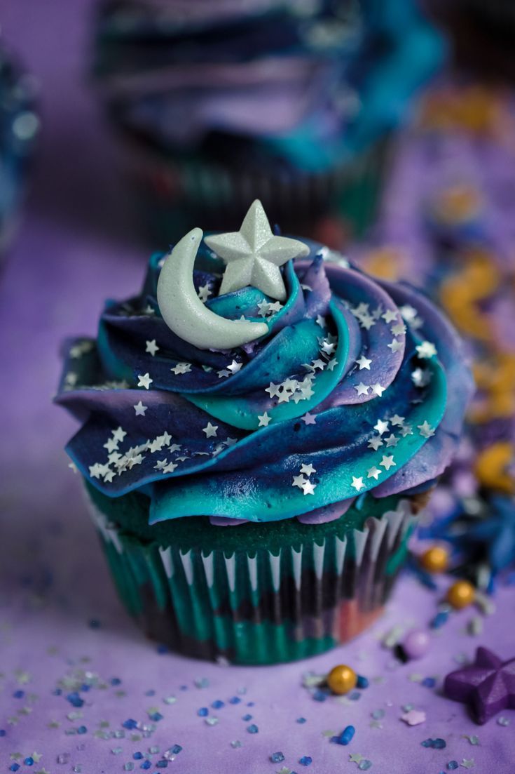 cupcakes decorated with blue icing and stars on a purple tablecloth covered in confetti