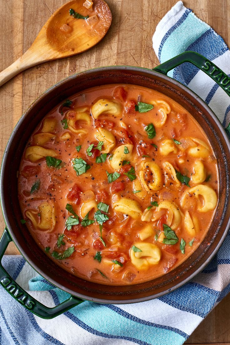 a pot filled with pasta and sauce on top of a wooden table next to a spoon