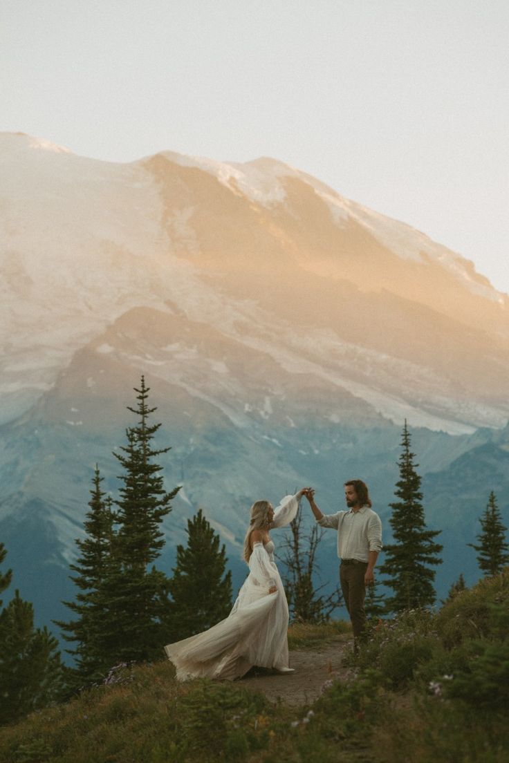 a man and woman standing on top of a mountain holding each other's hands