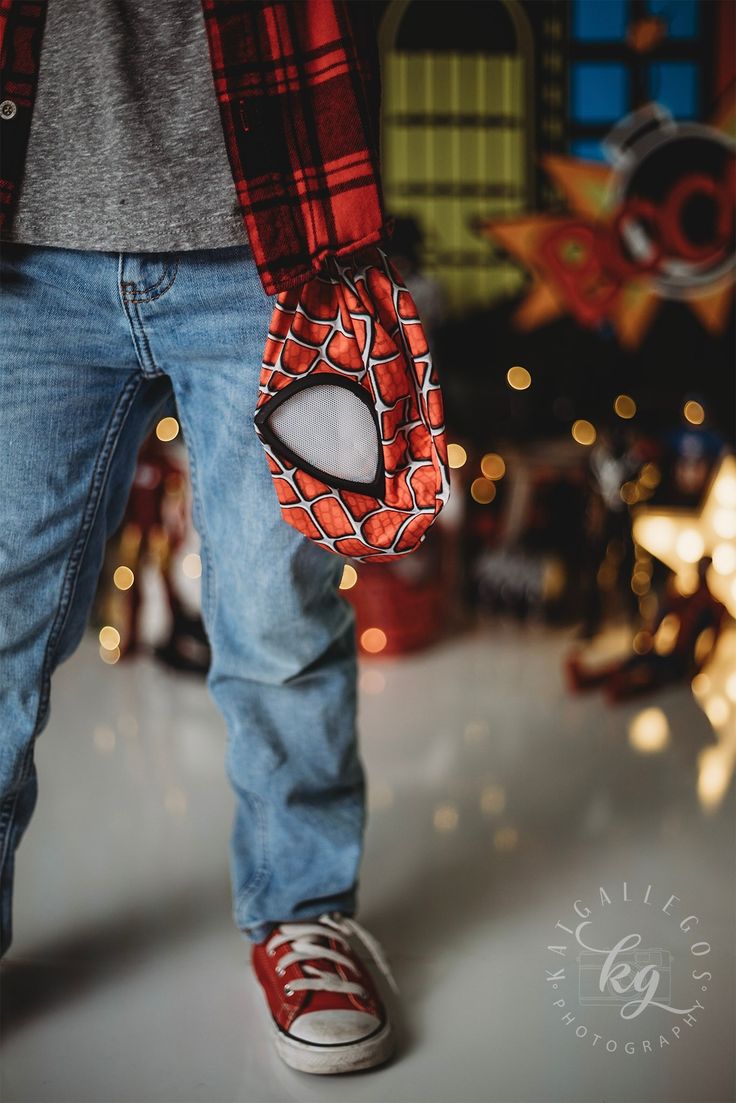 a close up of a person wearing red and black spider - man mitts, with christmas lights in the background