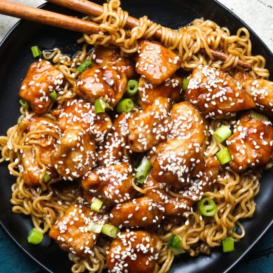 a black plate topped with noodles and meat covered in sesame seed sauce next to chopsticks