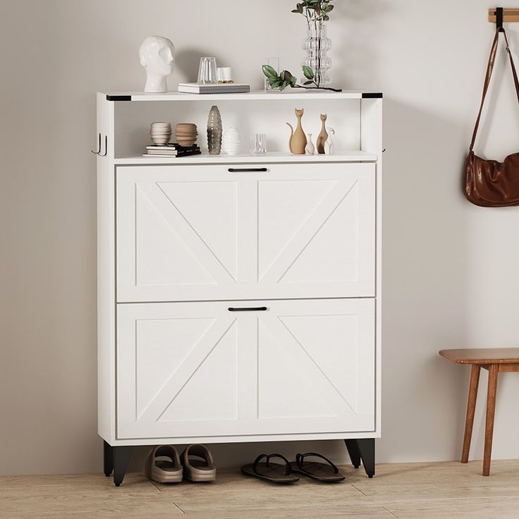 a white cabinet with two doors and shoes on it next to a wooden chair in a room