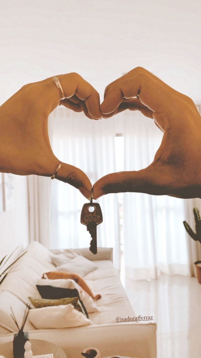 two hands making a heart shape over a couch with a house key in the middle