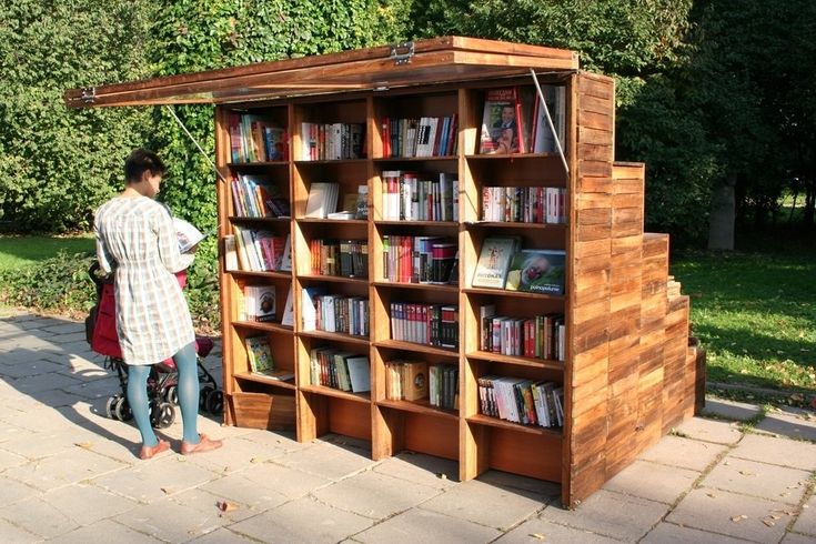 a man standing next to a wooden book case filled with books on top of a sidewalk