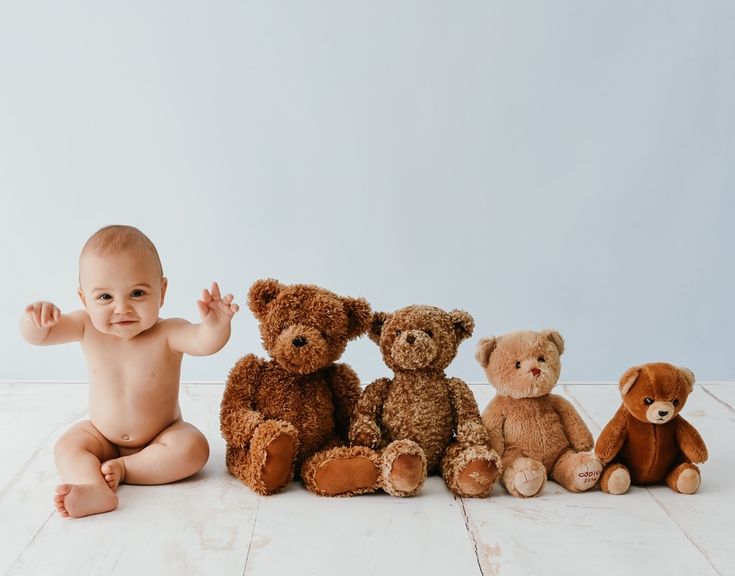 a baby sitting on the floor with five teddy bears in front of him and smiling at the camera