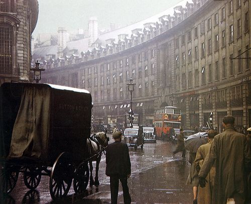 an old photo of people walking in the rain with horses and buggies on a city street