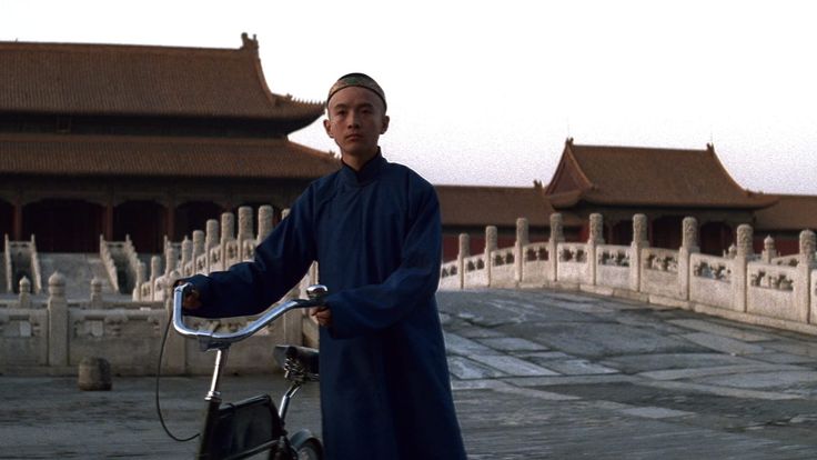 a man standing next to a bike in front of a building with lots of pillars