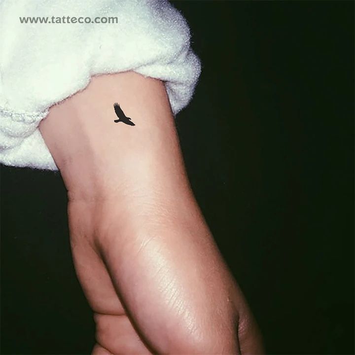 a small black bird tattoo on the left wrist and right hand with a white towel over it