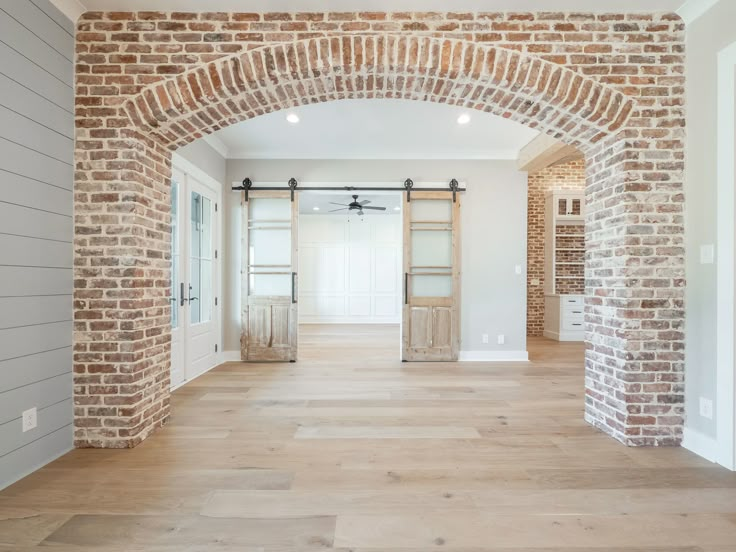 an empty room with wooden floors and brick arches on the wall, leading into another room