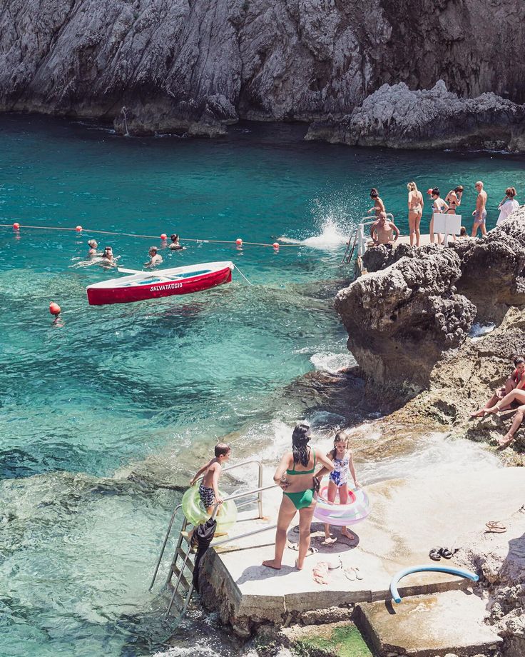 many people are swimming in the water near some rocks and cliffs, while others watch