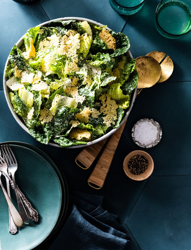 a bowl filled with broccoli on top of a wooden table next to silverware