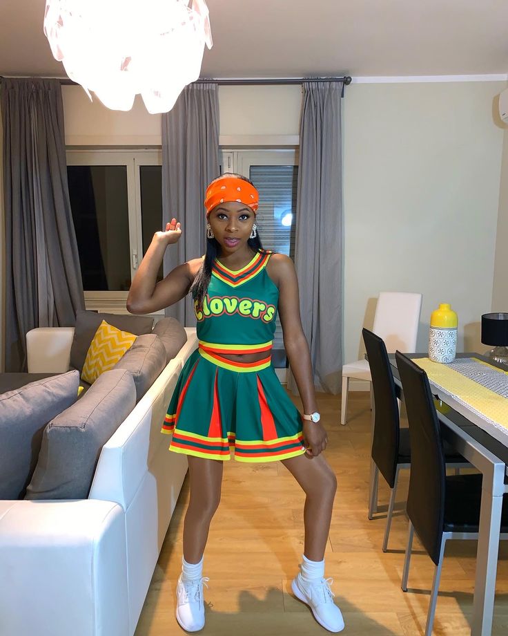 a woman in a green and red cheerleader dress standing in front of a couch