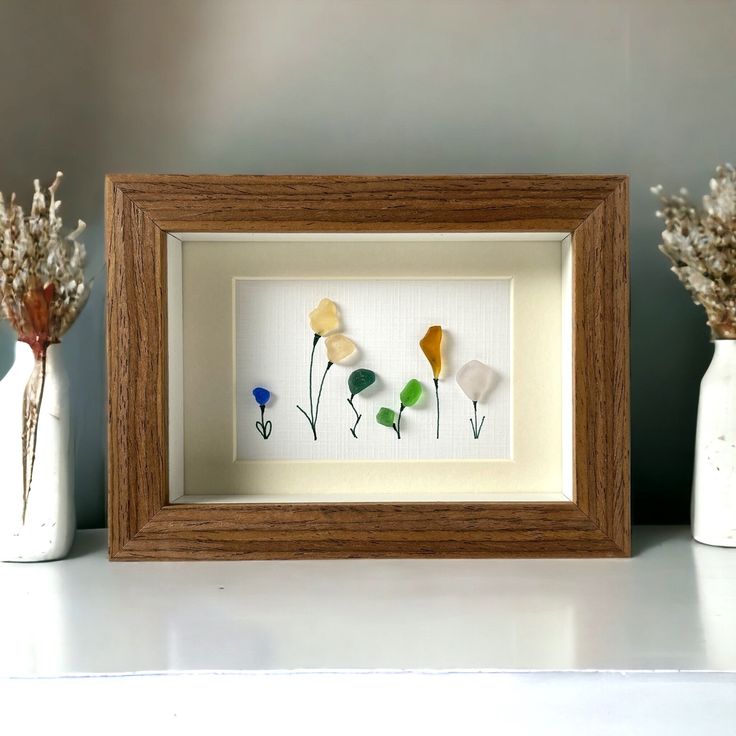 three dried flowers in vases sitting on a shelf next to a framed artwork piece