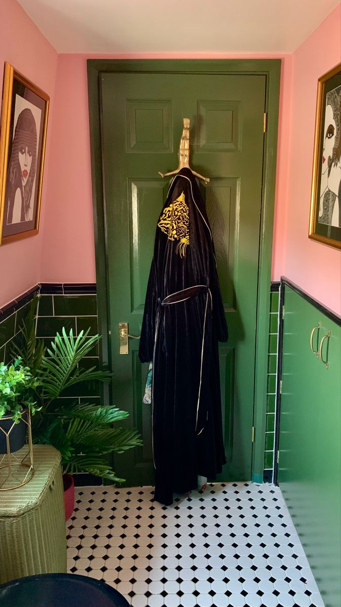 a black robe hanging on a green door in a pink and white tiled room with potted plants