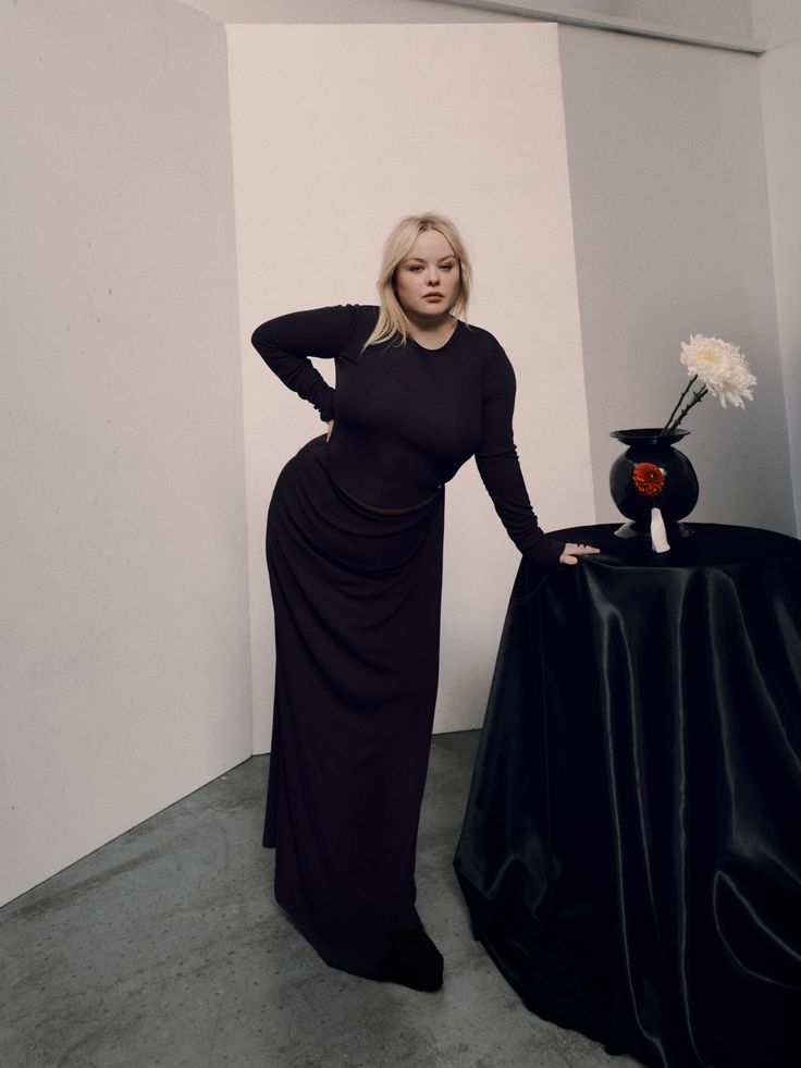 a woman standing next to a table with a vase on it